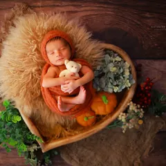 This autumn-themed setup features a baby sleeping soundly in a heart-shaped bowl, surrounded by tiny pumpkins and berries. We use natural elements and textures to create a warm, organic feel for our newborn photography.