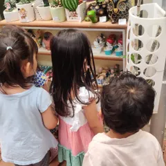 Three children curiously examine decorative garden gnomes and colorful pots at the nursery.