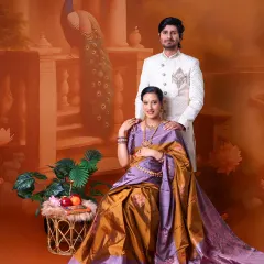 A regal portrait of the expecting couple. The mom-to-be is seated, draped in a beautiful saree, while her partner stands by her side, set against a traditional painted backdrop.