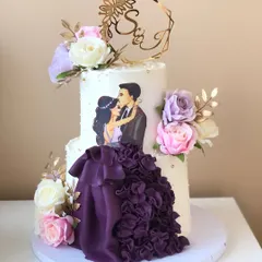 A dramatic two-tiered engagement cake with a custom illustration of the couple. The ruffled purple gown detail is handcrafted from fondant.
