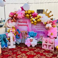 A clear, centered shot of the naming ceremony backdrop. The design includes a crescent moon balloon, a crown accent, and "BABY" blocks, all tied together with a pink and gold color scheme.