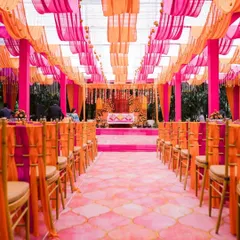 An explosion of pink and orange, this mehendi decor transforms the space into a vibrant paradise. The draped ceiling, patterned aisle, and coordinated chair ties show a commitment to a cohesive and joyful theme.