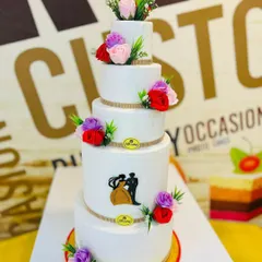 This grand 10kg, five-tiered wedding cake is a perfect example of classic elegance. Each tier is finished with smooth white fondant and decorated with delicate, colorful sugar flowers and a silhouette of a couple, showcasing our ability to create large, stunning cakes for your most important day.