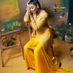 A model posing artistically in a vibrant yellow embroidered jacket and palazzo set. The image captures the feeling of fashion as a form of art.