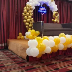 A side view of the anniversary stage, highlighting the half-arch design with a cascade of golden balloons on one side and white on the other.