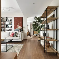 The open-plan living area in our 'Ikigai Living' project. We used a neutral color palette and minimalist furniture, including open-back metal and wood shelving, to create a bright, gallery-like space that showcases the client's art collection.