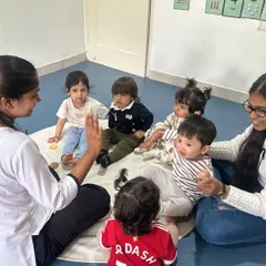 Toddlers and teachers sit in a circle for a group activity, learning social skills like taking turns and listening to others.