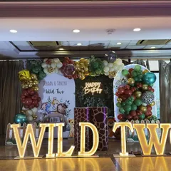 When the theme is "Wild Two," we go all out. This jungle safari setup for twins Vihaan and Vaniya features a lush green foliage backdrop, a custom balloon arch with animal print accents, and bold, illuminated "WILD TWO" marquee letters that set the stage for a roaring good time.