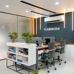 This angle highlights the custom workstations and ergonomic seating chosen for the Indirapuram office. The frosted glass partition on the left provides privacy for an adjoining cabin, while the "Teamwork" wall graphic reinforces a collaborative company culture.