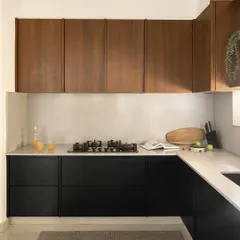 A view of the L-shaped kitchen layout, showcasing the contrast between the dark lower cabinets and the warm wood tones of the upper cabinets. The design is minimalist yet highly functional.