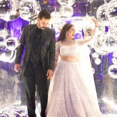The bride and groom against a backdrop of disco balls. Her glamorous white lehenga and sparkling makeup were perfect for this fun, high-energy sangeet night.