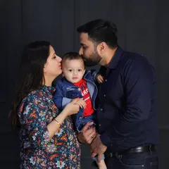 A tender moment between parents and their son. The father's kiss on the baby's head is a sweet, candid gesture that adds warmth to this classic studio portrait.