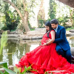 A quiet, tender moment by the water. The way this couple is posed, nestled together in a lush park setting with the vibrant red of her gown, creates a feeling of intimacy and peaceful anticipation.