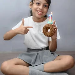 Celebrating a tenth birthday with a donut instead of a cake. This fun studio-style shoot captures the personality of the birthday girl, focusing on her happy expression as she points to the number 10 candle.