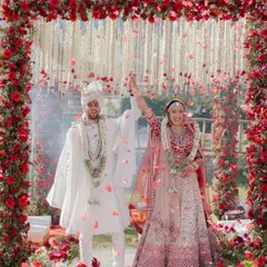 An intimate wedding ceremony in the mountains, where the couple celebrates their union under a shower of rose petals, framed by a vibrant red floral arch.