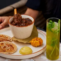 Our signature Champaran Mutton, plated with Sattu Parantha, roasted garlic, and a sharp mustard chutney. The mutton is slow-cooked in a sealed pot with rustic spices, creating a dish that is both robust and tender.