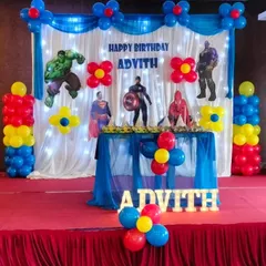 A classic Avengers theme decoration for Advith. This setup features a simple white curtain backdrop with fairy lights, cutouts of superheroes like Captain America and Hulk, and balloon pillars in primary colors.