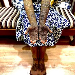 A full view of a bride showing off her beautifully stained mehendi on both hands and feet. The dark color signifies the deep love in a marriage and looks stunning in photos.
