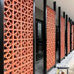 These terracotta jali brick panels, framed in black metal, create a visually striking and functional wall. The design allows for natural airflow and light while providing privacy, blending traditional materials with a modern aesthetic.