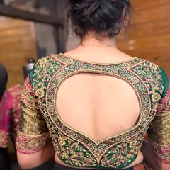 A unique heart-shaped open back design on a green bridal blouse. The entire piece is covered in detailed zardosi and threadwork, blending traditional craftsmanship with a modern silhouette.