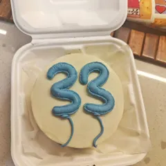 A close-up of a birthday bento cake in its takeaway box. The number "33" is piped to look like balloons, making it a fun and modern design.