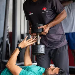 A trainer assists a client with a heavy dumbbell press, providing the support needed to complete the final reps of a challenging set.