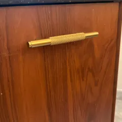 A detail shot of a knurled brass handle on a wooden cabinet. This small but significant element adds a touch of industrial luxe and a tactile quality to the furniture.