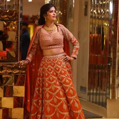 A stunning bright orange lehenga with intricate gold embroidery. This rental outfit is perfect for making a vibrant statement at a mehendi or sangeet ceremony.