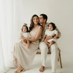 A sweet kiss for mom from dad while they hold their twin girls. This candid family photoshoot captures a moment of love and happiness.