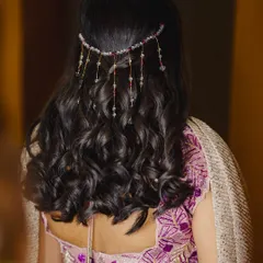 A beautiful hairstyle for a Sangeeth or reception. This look features soft, open curls adorned with a delicate, dangling hair accessory.