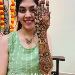 A smiling bride proudly displays her personalized mehendi, featuring the couple's initials "KR" clearly visible on the palm.