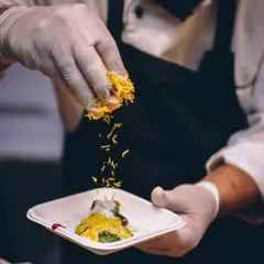 A chef sprinkles a final garnish on a plate of Indian chaat, adding texture and flavour.