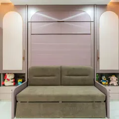 This room features a comfortable sofa that is part of a larger Murphy bed unit. The surrounding cabinetry, with its arched motifs and soft colors, provides ample storage for toys and books, making it a perfect kids' room or guest room.
