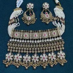 I love the craftsmanship on this antique finish choker set. The design has very detailed work with ruby-colored stones and is paired with beautiful chandbali earrings and delicate pearl strings, giving it a complete and traditional look.