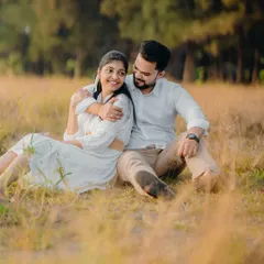 A candid moment of Milan and Pranali sitting in a field of tall grass. The warm, golden hour light makes this outdoor pre-wedding shot feel incredibly romantic.
