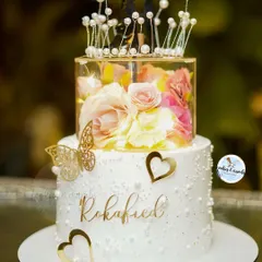 A beautiful two-tier cake for a Roka celebration. The clear spacer tier filled with flowers and fairy lights adds a touch of magic, making it a truly unique centerpiece for the happy couple.