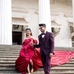 A fairytale moment captured on the steps. The bride-to-be wears a deep maroon gown with a long trail, complemented by her partner's matching maroon tuxedo.