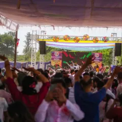 A view from the back of the crowd at a massive Holi party. The energy is contagious, with everyone's hands in the air.