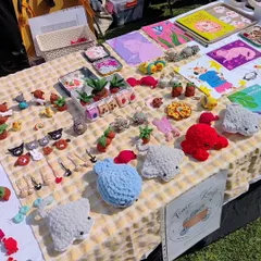 Another angle of my market stall, showing the full range of my handmade accessories. You can spot the fluffy crochet stingrays, tiny potted plants, and a wide selection of my cross-stitch pins and keychains ready for new homes.