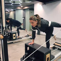 This client is performing a single-leg plank on the Reformer, a move that challenges balance and deeply engages the core muscles. The mirror reflection shows her focused alignment.
