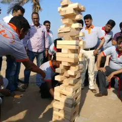 A team-building exercise in action with a very tall Giant Jenga tower at a corporate beach event. This game is excellent for fostering communication and teamwork.
