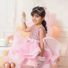 A little princess in a beautiful, fluffy pink dress smiles brightly during her birthday celebration, surrounded by festive pastel balloons and a birthday cake.
