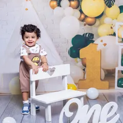 A duplicate of image 13, showing a smiling one-year-old boy in a charming birthday setup. The yellow and green balloons create a fresh and joyful atmosphere for his milestone photo.