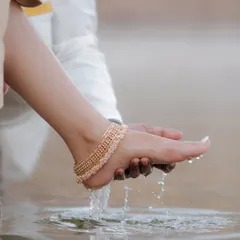 An artistic and symbolic close-up of a groom washing his bride's feet in the water of a temple pond, a beautiful gesture of love and respect.