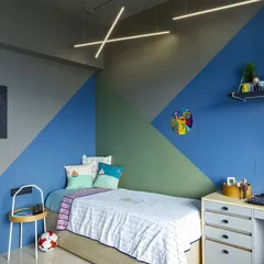 A bedroom for a young adult, featuring a cool geometric color-blocked wall. The design includes an expandable bed for sleepovers and a compact study desk.
