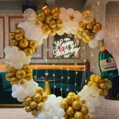 A classic and celebratory ring backdrop in gold and white. This setup is perfect for an adult birthday, featuring a neon sign, fairy lights, and a champagne bottle foil balloon.