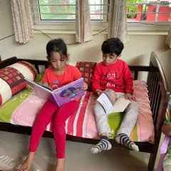 Two children share a quiet moment on a comfy bench, reading their books side by side. Our library encourages both independent and shared reading experiences.