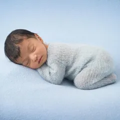 The perfect sleepy pose. A newborn in a soft blue sleeper is curled up on a simple, matching blue blanket, showcasing their peaceful slumber.
