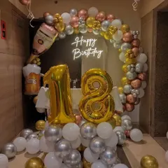 A festive 18th birthday decoration with a balloon arch in gold, silver, and white. The theme is enhanced with champagne bottle and beer mug foil balloons.