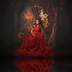 Seated on a floral swing, this portrait in a magnificent red ruffled gown is a celebration of life and joy. The dark, painterly backdrop makes the vibrant color pop, creating a piece of fine art.